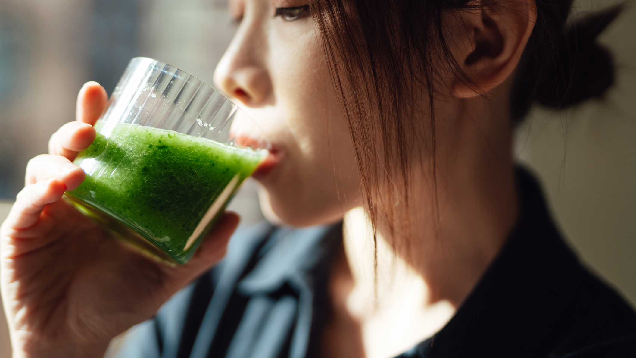 oung Asian woman drinking a glass of Terra Health Essentials supergreens powder